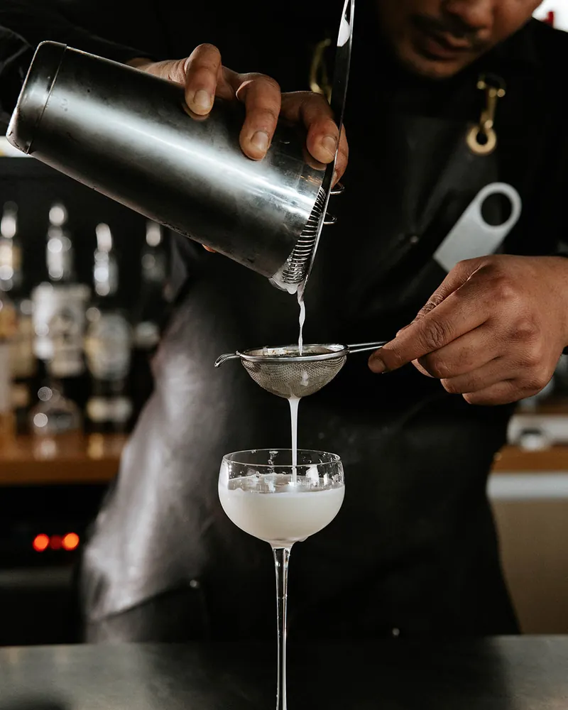 Cocktail being poured into a coupe glass at Times of India